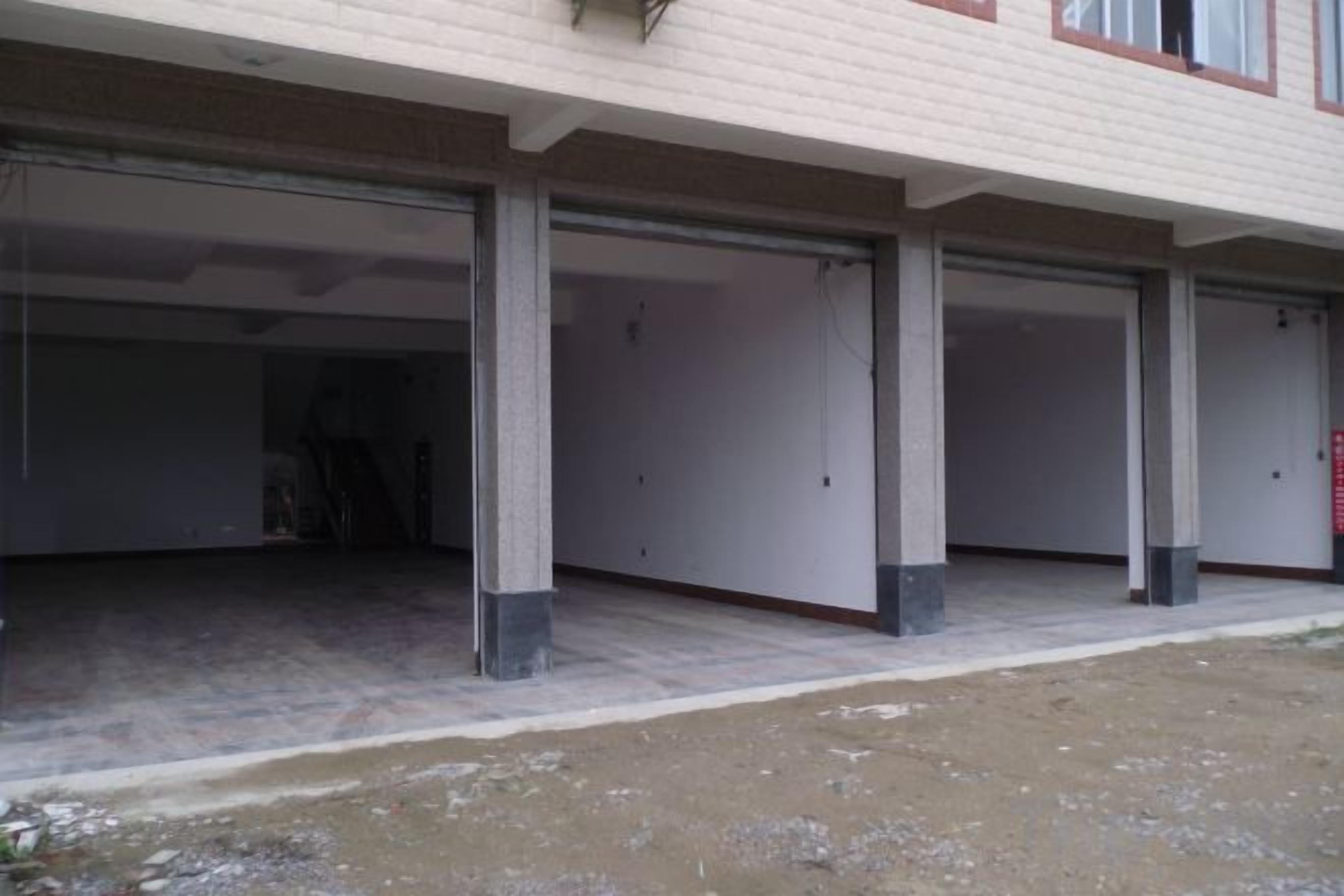 Um edifício com várias entradas tipo garagem, pilares de concreto e terreno de terra.