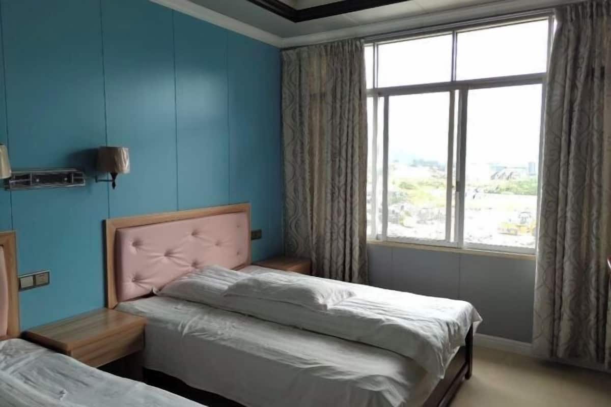 A bedroom with a bed, a nightstand, a window with curtains, and a view of the outside.