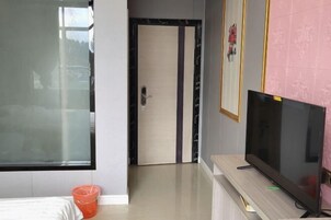 Habitación de hotel con un ventanal grande, una puerta con diseño a rayas, un televisor sobre un soporte de madera y un cesto de basura naranja pequeño.