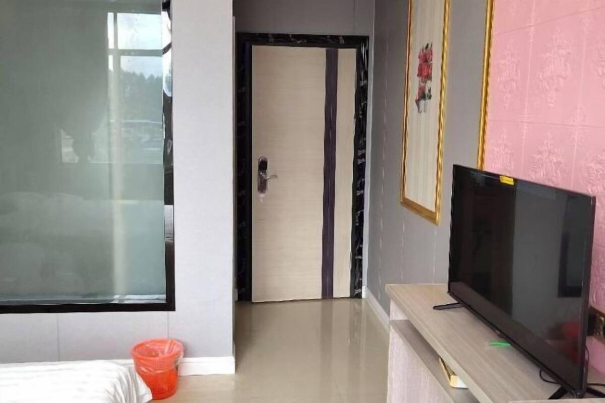 A room with a large window, a door, a television on a stand, and a small orange container on the floor.