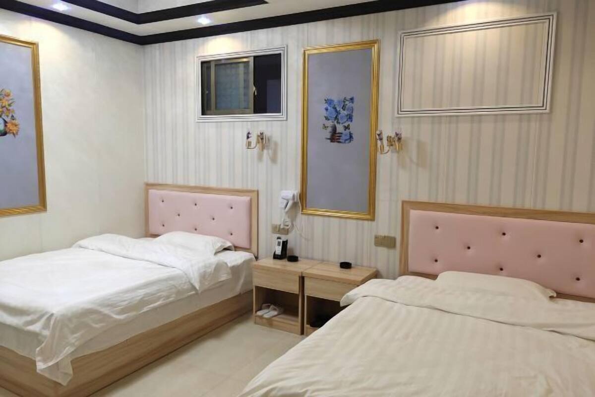 A hotel room with two beds, a small desk, and a window.