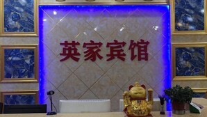 A reception desk with a marble wall, a golden statue, and a blue-lit sign. - Yingjia Hotel (Zhongshan)