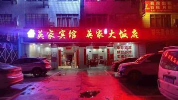A hotel with a neon sign in red and yellow, multiple parked cars, and a visible entrance.