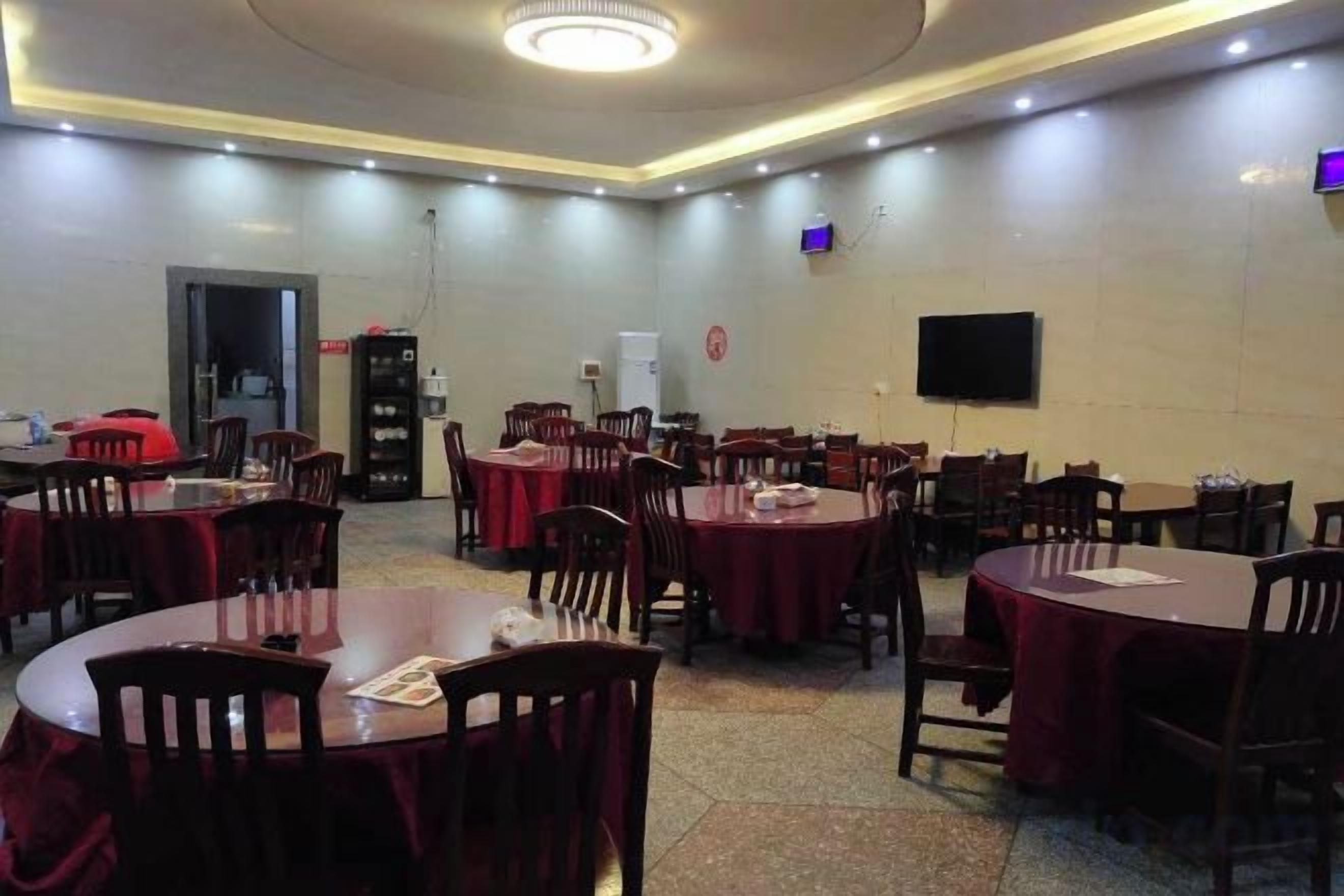 A dining area with round tables and chairs, a flat-screen TV mounted on the wall, and a fire extinguisher.