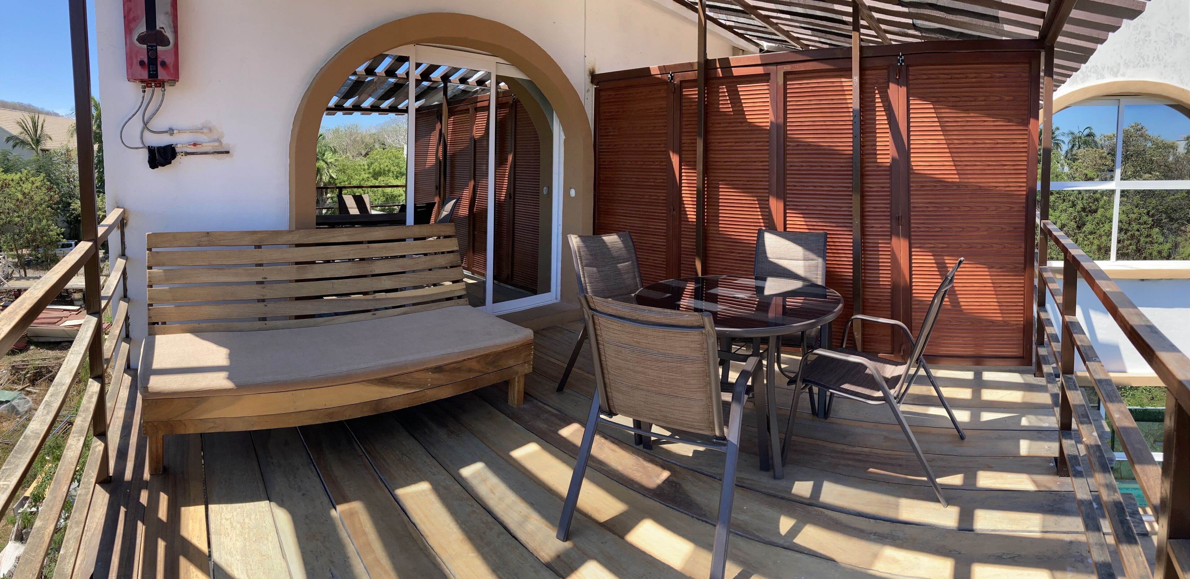 An outdoor patio with a wooden bench, a table with chairs, and a pergola providing shade.