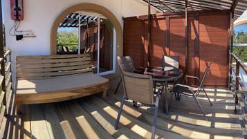 An outdoor patio with a wooden bench, a table with chairs, and a pergola providing shade.