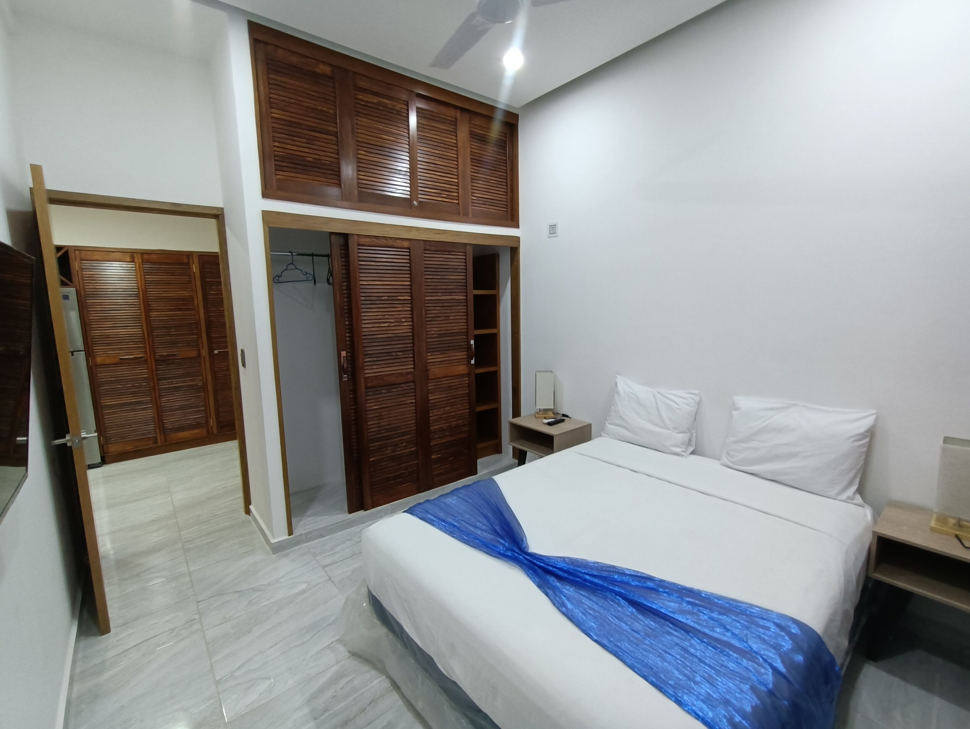 A bedroom with a bed, white pillows, a nightstand, a wooden wardrobe, and a mirror.