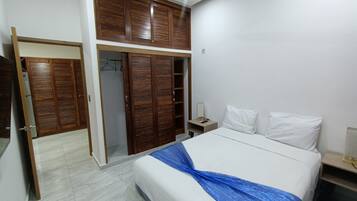 A bedroom with a bed, white pillows, a nightstand, a wooden wardrobe, and a mirror.
