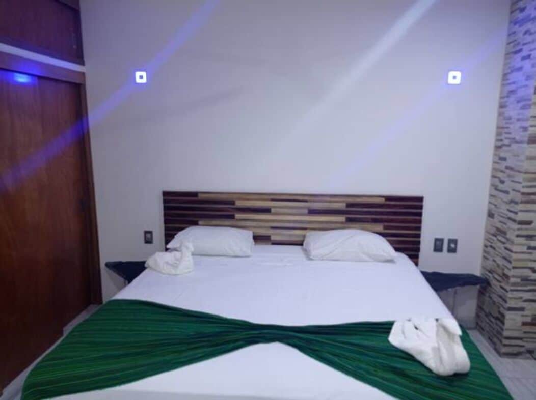 A hotel room with a bed, a green bedspread, and a wooden headboard.