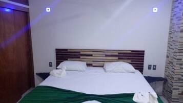 A hotel room with a bed, a green bedspread, and a wooden headboard.