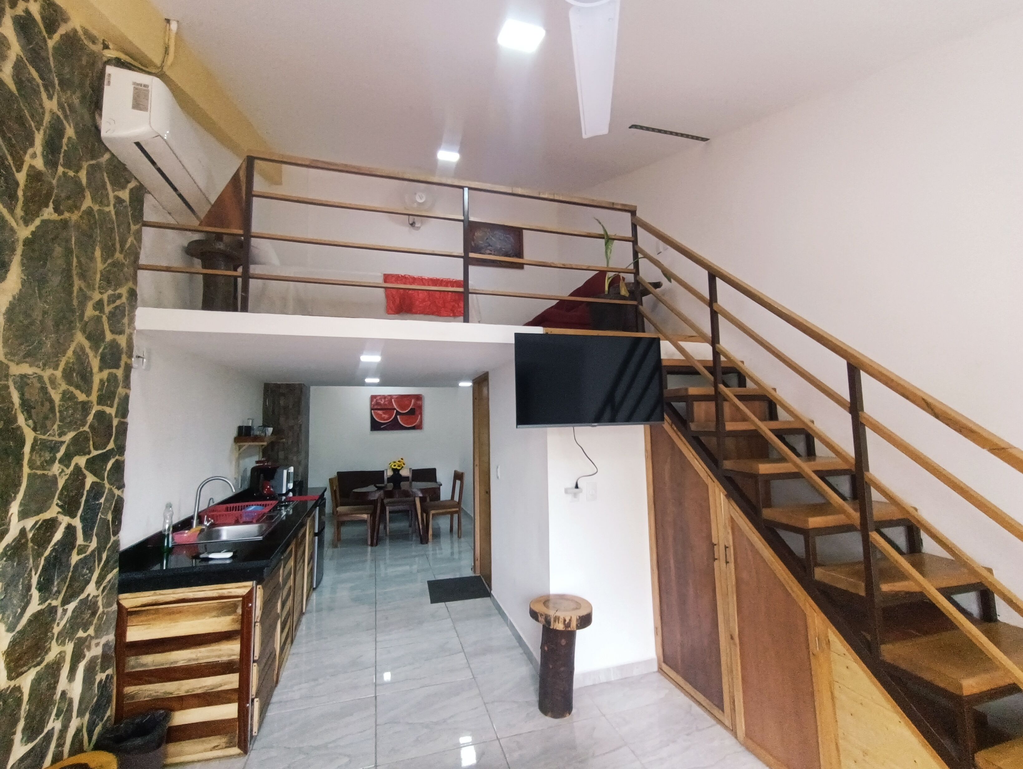 A spacious kitchen with a dining area, a staircase, and a TV mounted on the wall.