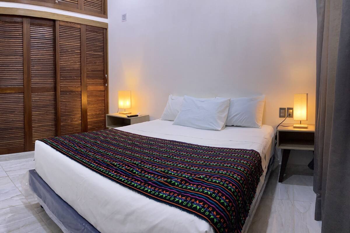 Quarto com cama, luminárias de cabeceira, guarda-roupa e televisão.