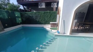 En swimmingpool med en klar blå vandlinje, omgivet af en hvid mur og en grøn hæk.