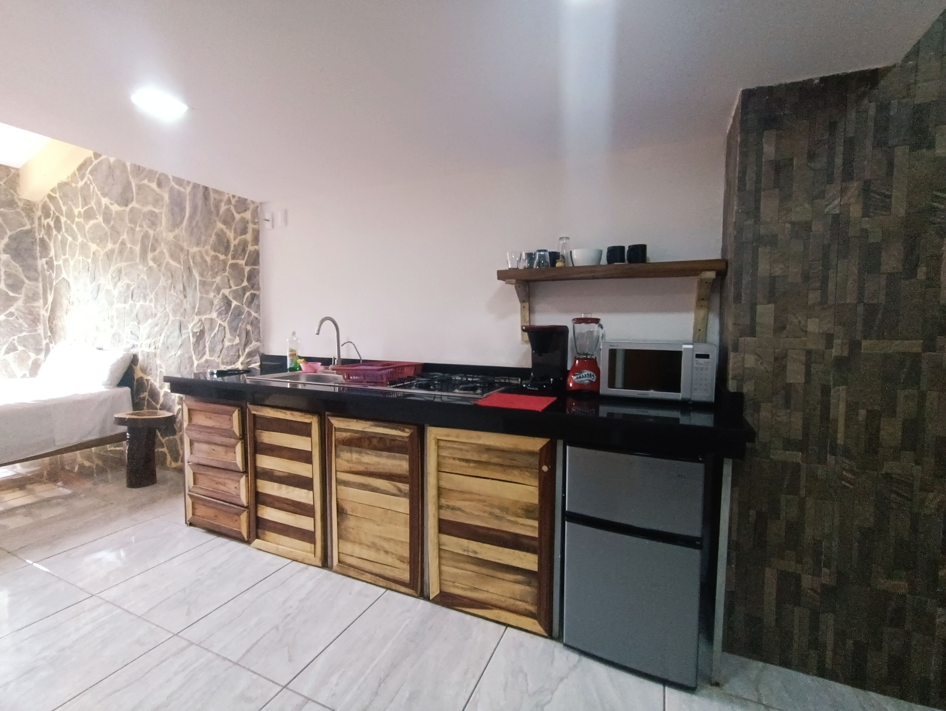 A modern kitchen with a stone accent wall, wooden cabinets, and a compact refrigerator.