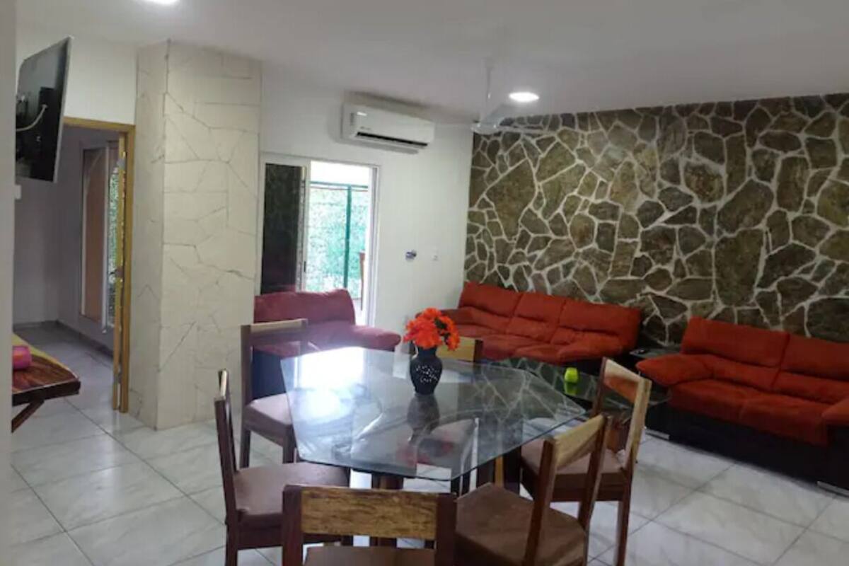 Uma área de refeições com mesa de vidro, sofás vermelhos e parede de pedra.