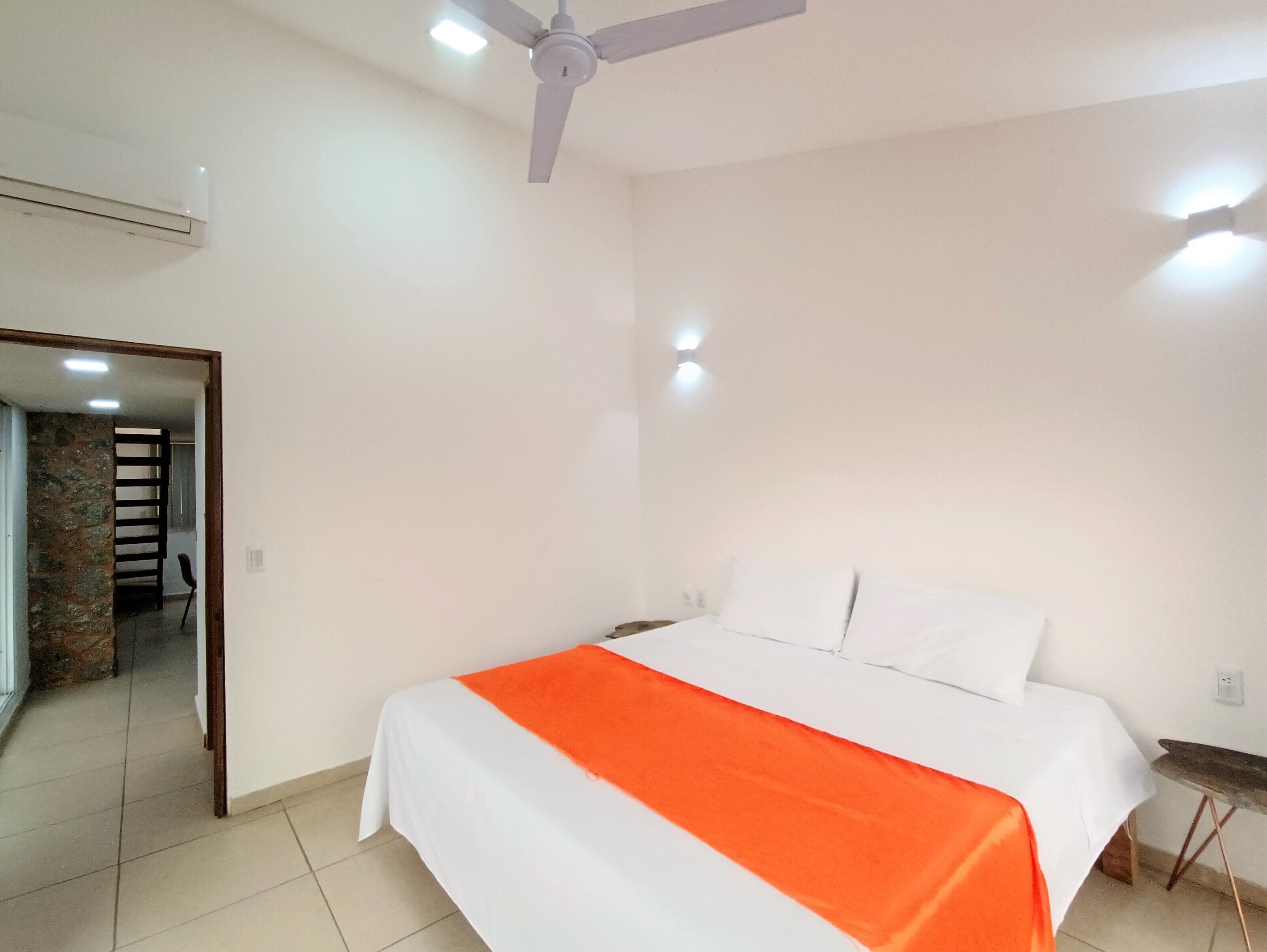 Une chambre à coucher avec un lit, des murs blancs, un ventilateur de plafond et une petite table.