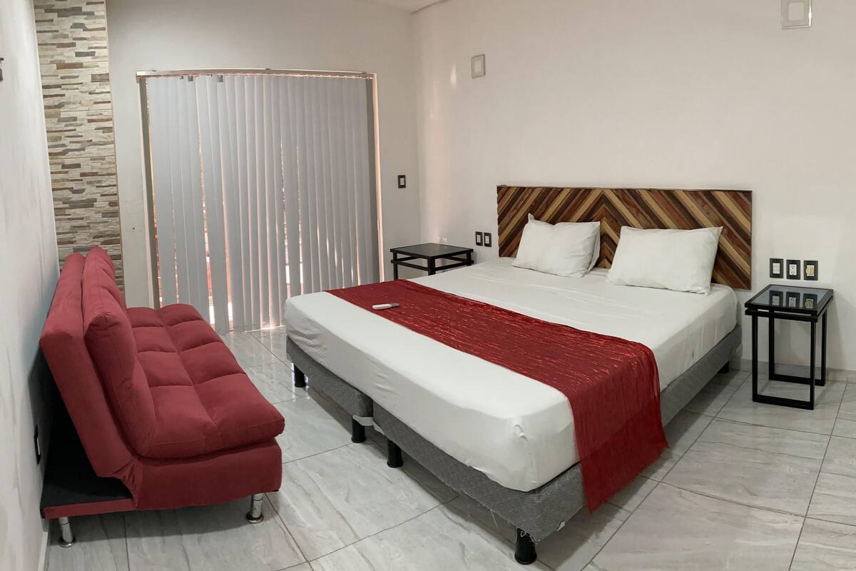 Um quarto moderno com uma cama, uma cadeira vermelha, uma mesa de cabeceira e um guarda-roupa.
