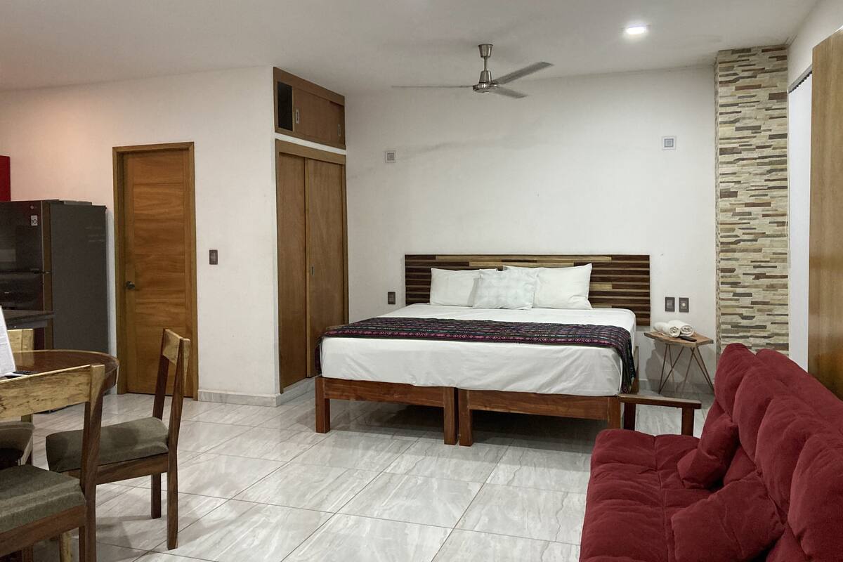 Um quarto com cama, guarda-roupa de madeira, ventilador de teto e sofá vermelho.