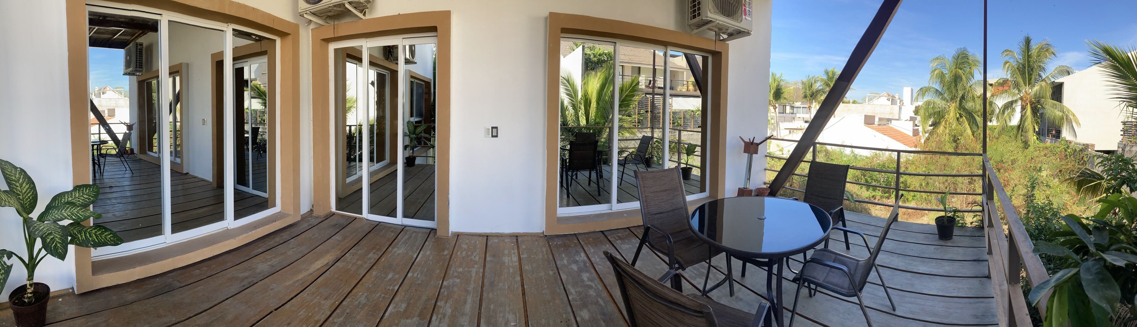 A wooden deck with a glass door leading to a balcony, a round table with chairs, and a potted plant.