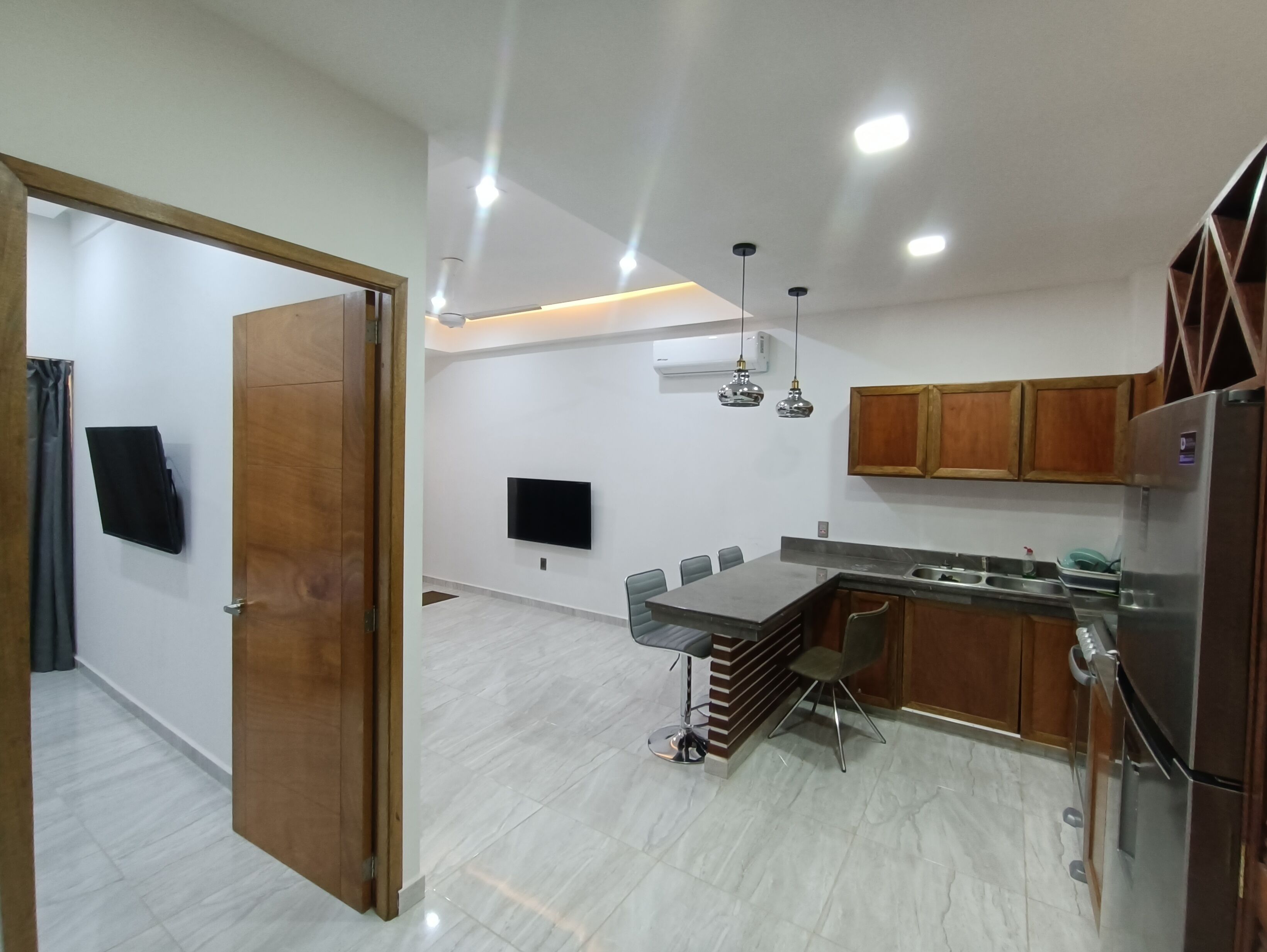 A modern kitchen with a dining area, wooden cabinets, a built-in oven, and a flat-screen TV.