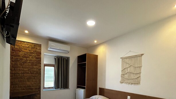 A hotel room with two beds, a stone wall, an air conditioner, a TV mounted on the wall, and a macrame wall hanging.