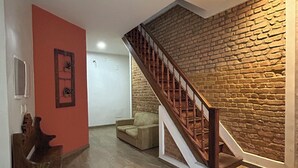 A staircase with a wooden handrail leading to a landing with a stone wall. A beige sofa is placed on the landing, and a wooden bench is visible in the foreground.