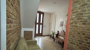 A spacious living area with a high ceiling, a wooden staircase, and a brick wall.