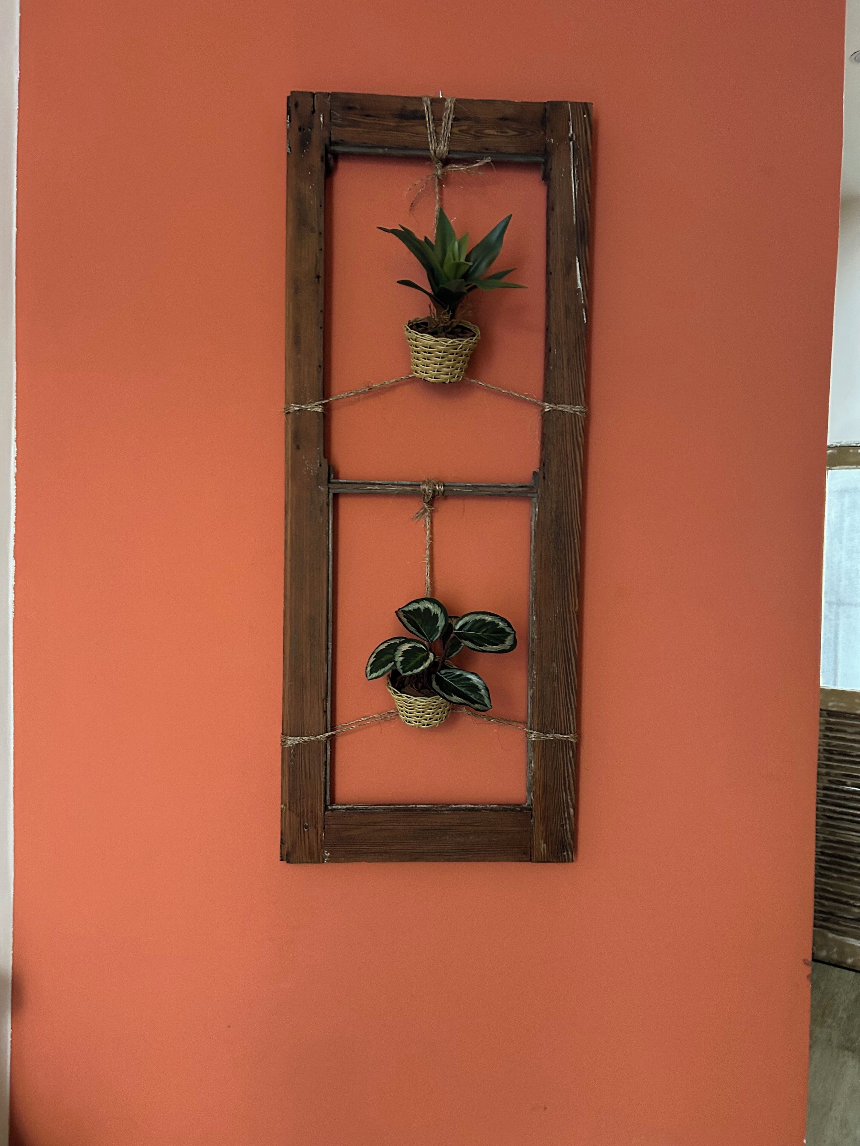 A wall-mounted wooden frame with two potted plants hanging from it.