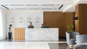 Un espace d’accueil moderne, doté d’un comptoir de réception en marbre, de lambris en bois et d’une grande plante en pot.