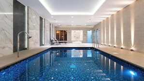 Une piscine intérieure moderne, avec un sol carrelé, un espace détente avec des chaises et un comptoir d'accueil en arrière-plan.