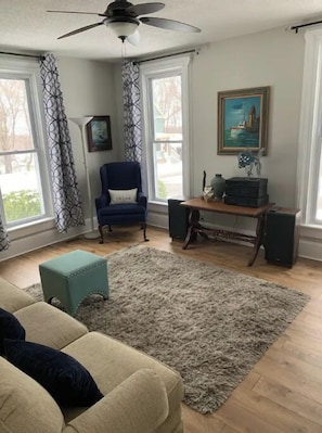 Relax in this inviting living room with a sofa, armchair, and ottoman, surrounded by a framed painting and books on a small table.