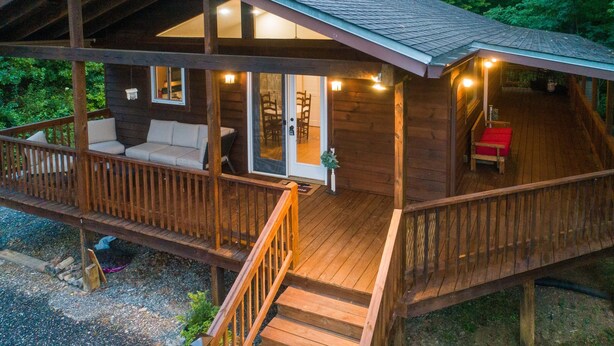 Una cabaña de madera con un porche, una zona de estar al aire libre techada y una escalera que lleva a la entrada.