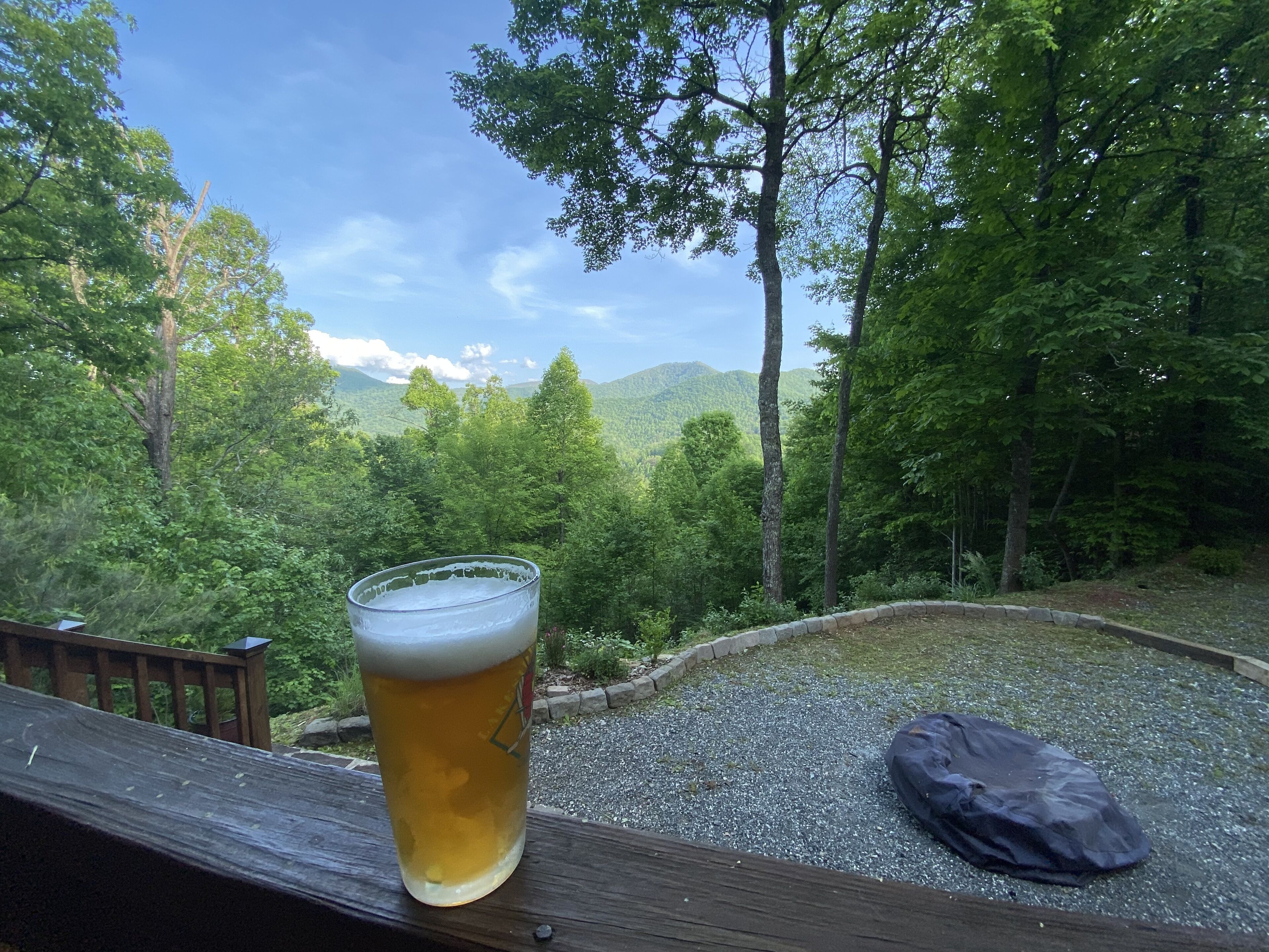 Ein Bierglas auf einer Holzterrasse mit Blick auf einen Wald und Berge.