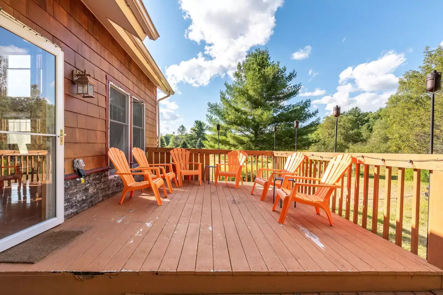 Een houten terras met oranje Adirondack-stoelen, een stenen muur en een glazen deur die naar een kamer leidt.