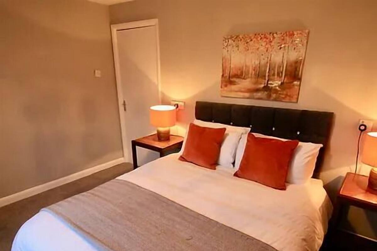 A neatly made bed with a striped blanket, two bedside tables with lamps, and a painting on the wall.