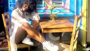 Una persona sentada a una mesa de madera con una silla, una pequeña planta en maceta y un vaso de agua sobre la mesa.