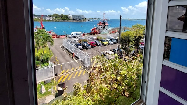 Vista desde una ventana sobre un puerto con barcos, una grúa y coches aparcados.