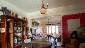 Un comedor con suelo a cuadros, una mesa de madera y sillas. Hay una estantería llena de libros y objetos decorativos. Un candelabro cuelga del techo, y una alfombra roja cubre el suelo.