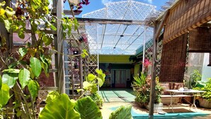 Un espacio al aire libre cubierto con techo transparente, rodeado de plantas diversas y suelo de baldosas.