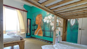 Una habitación con cama, un banco de madera, un mural y vista al mar.