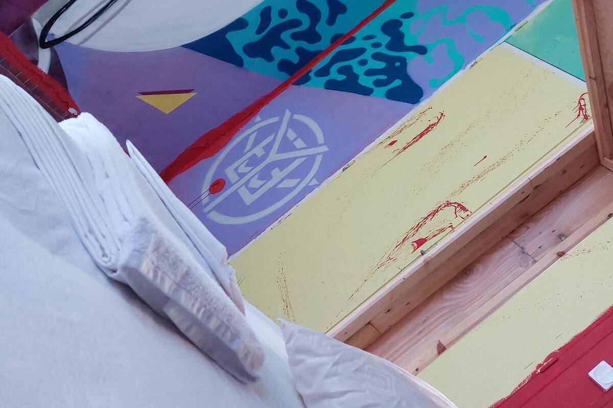 Una habitación con una cama, cabecera de madera y un mural de pared colorido.