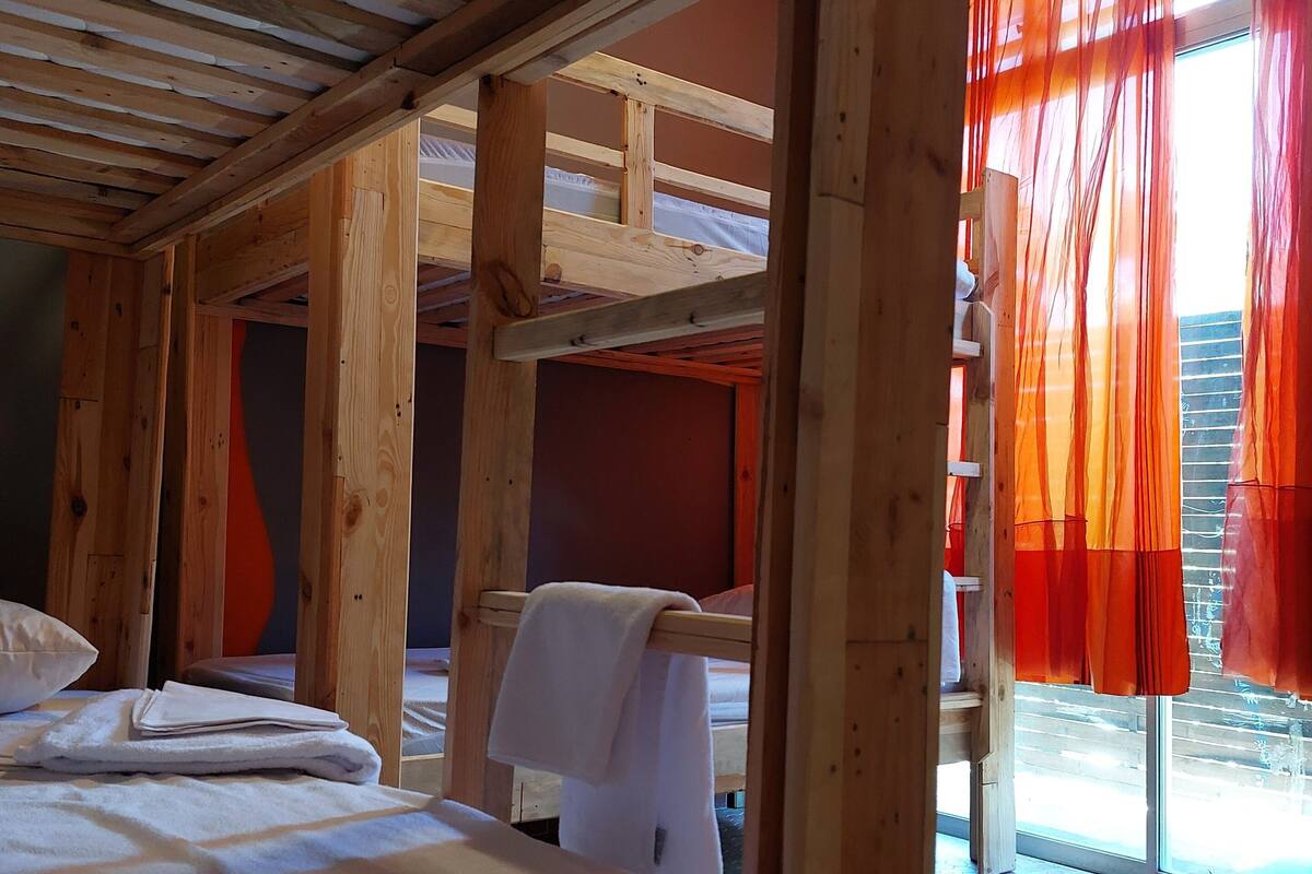 Una habitación de madera con literas, una ventana con cortinas naranjas y suelo de baldosas.