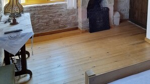 Ein rustikaler Raum mit Kamin aus Stein, Holzbalken und einem Tisch mit Lampe.