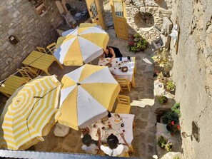 An outdoor dining area with yellow and white striped umbrellas, stone walls, and potted plants. - SARI KEÇİ TAŞ OTEL (Gökçeada)