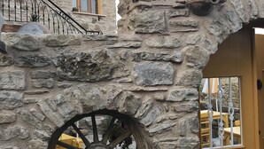 Ein Steinhaus mit gelber Tür, einem Fenster mit Blumenkasten und einer Steinmauer mit Wasserrad.