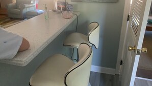 Een keukenhoek met een bargedeelte, barstoelen, een koelkast en een raam met gordijnen.