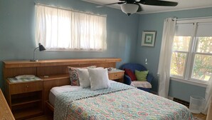 Een slaapkamer met een bed, nachtkastjes, een stoel, een raam met gordijnen en een plafondventilator.