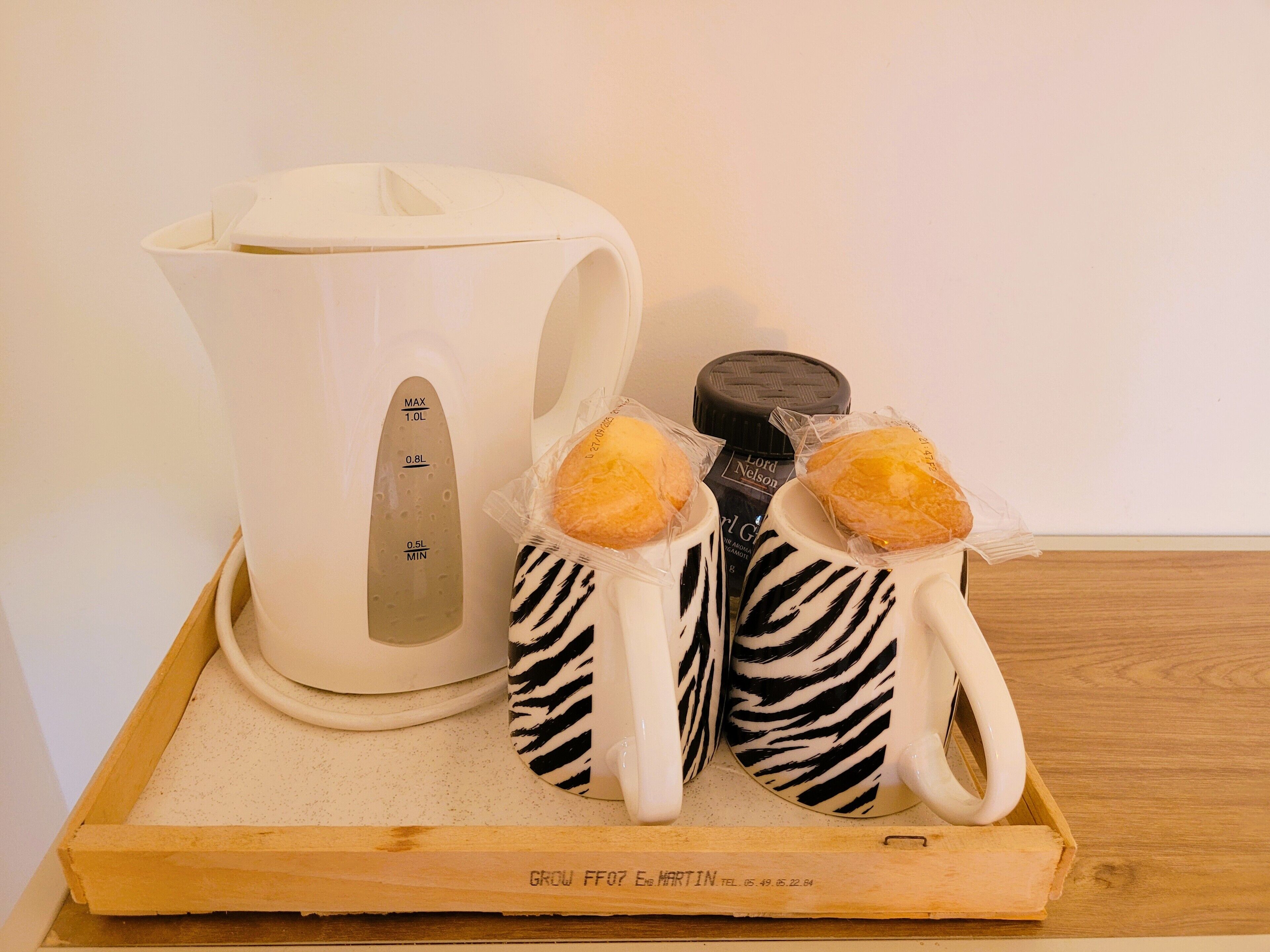 Un plateau avec une cafetière en céramique blanche, deux tasses à motifs zébrés et deux pâtisseries emballées.