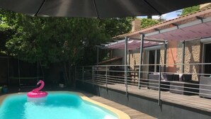 A swimming pool with a pink flamingo float, surrounded by a wooden deck and a covered patio area. - Allegria Nimes (Nîmes)
