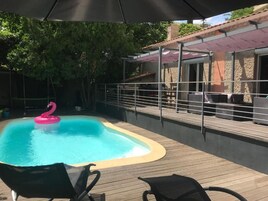 Una piscina con un flotador de flamenco rosa, rodeada por una terraza de madera y un área de patio techada.